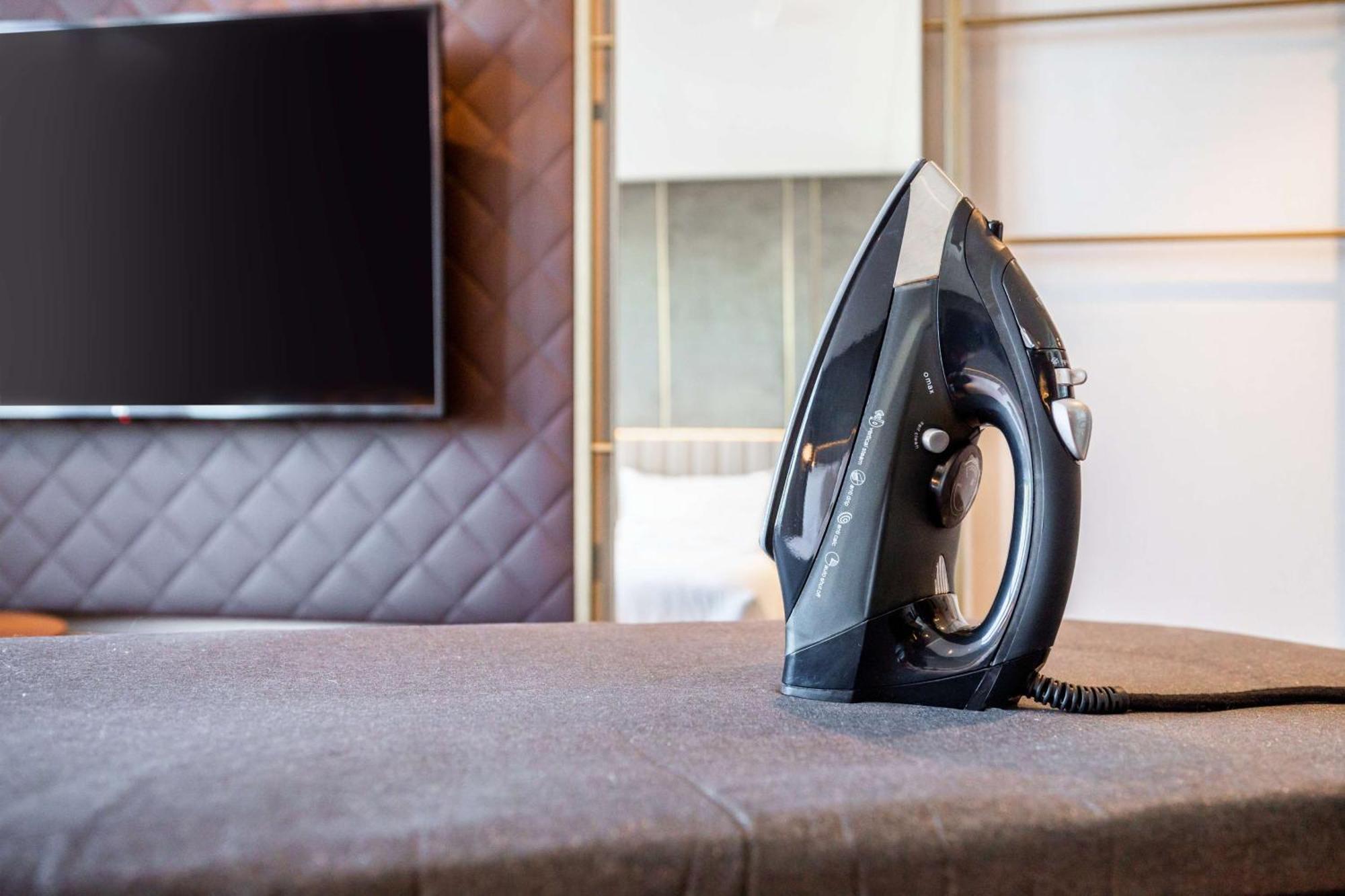 Nh Collection Copenhagen Hotel Kültér fotó The photo shows a black iron placed on a grey ironing board, which is covered with a fabric surface. In the background, there's a large television mounted on the wall, and the setting appears to be a modern room with stylish decor, featuring a quilte