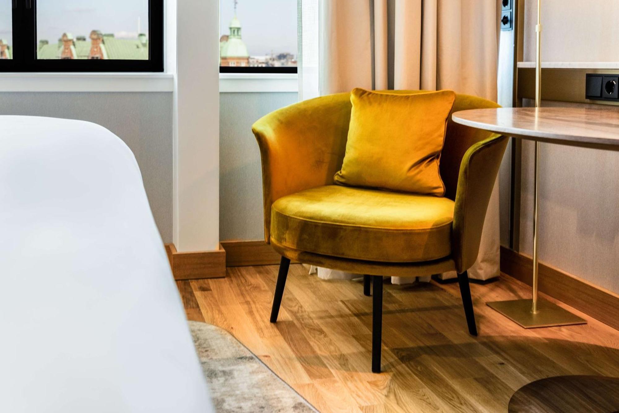Nh Collection Copenhagen Hotel Kültér fotó The photo shows a stylish interior space featuring a modern, round yellow armchair with a plush cushion, placed next to a small table. The chair has a contemporary design with slender legs. In the background, there are large windows with light curtai